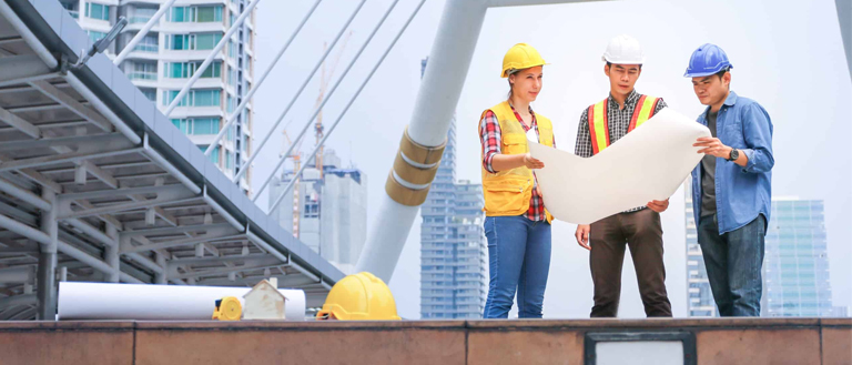 Three Students in Hard Hats Examining a Blueprint on a Bridge: Civil Engineering Homework and Assignment Focus Three students in hard hats standing on a bridge, examining a blueprint for their civil engineering homework and assignment