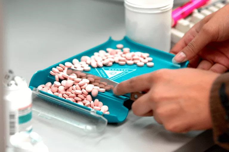 A person carefully cuts pills into a blue tray, completing a homework or assignment related to medication dispensing. A person cutting pills into a blue tray, a task related to a Online Dispensing Help