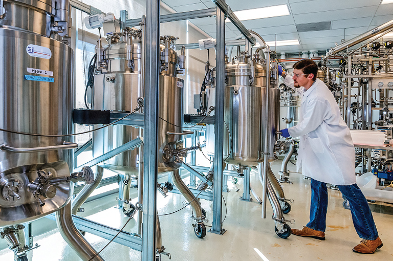 Industrial Biotechnology Assistance: Man in Lab Coat Standing in Front of Stainless Steel Tanks An image depicting a man in a lab coat standing in front of stainless steel tanks, representing industrial biotechnology assistance