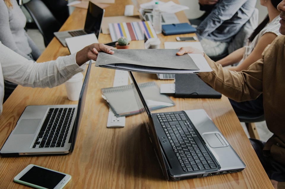 Management Consulting Homework: Students Engaged in Analysis and Research Two students holding papers at a table with laptops, appearing to be working on management consulting homework and assignment and seeking assistance