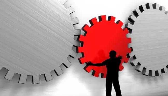 Operation Management: Analyzing Efficiency with the Red Gear Wheel A man stands before a red gear wheel, representing the concept of operations management assignment help