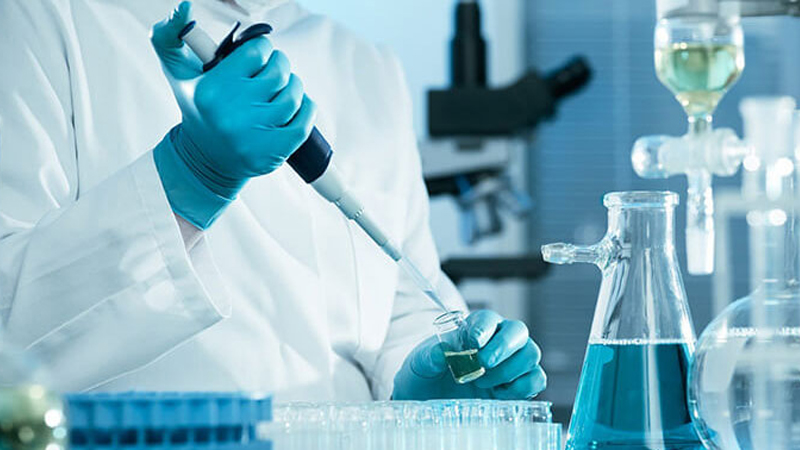 Pharmaceutical Student Conducting Lab Experiment for completing their pharmaceutical chemistry Assignment Lab-coated pharmaceutical student experimenting, holding a test tube as part of a pharmaceutical chemistry assignment help