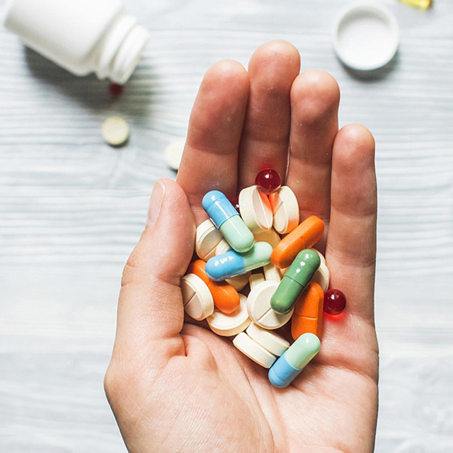 Navigating the Complexities: Your Guide to Pharmacology Assignment Help A person holds a variety of pills and capsules in their hand with a pill bottle in the background on a light-coloured surface, illustrating the complexities often faced when seeking pharmacology assignment help